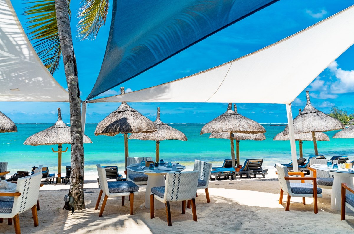 Constance Belle-Mare Plage Hotel front beach restaurant with Tables, chairs set and shade sails. Beautiful setup for lunch on the beach with turquoise sea. Constance Mauritius Hotel Image Download