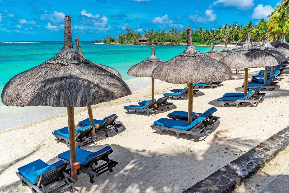 4K Mauritius Desktop Wallpaper. Constance Belle-Mare beach with straw umbrellas, blue hotel deckchairs and palm trees in the background. Calm and turquoise sea during the day. Constance Mauritius Hotel Image Download